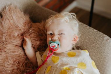 baby with a pacifier lying on a sofa