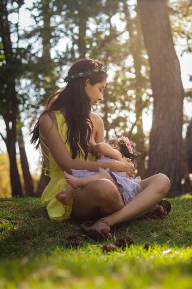 mother breastfeeding while sitting on grass