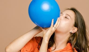 woman blowing up a blue balloon